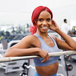 Jazzmyne Rain, a young Black woman with long red curly hair, confidently works out at local gym during her lifestyle branding session. She is wearing a sleek blue sports outfit, friendly expression, lifestyle, brand photoshoot.