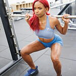 Jazzmyne Rain, a young Black woman with long red curly hair, confidently works out at local gym during her lifestyle branding session. She is wearing a sleek blue sports outfit, friendly expression, lifestyle, brand photoshoot.